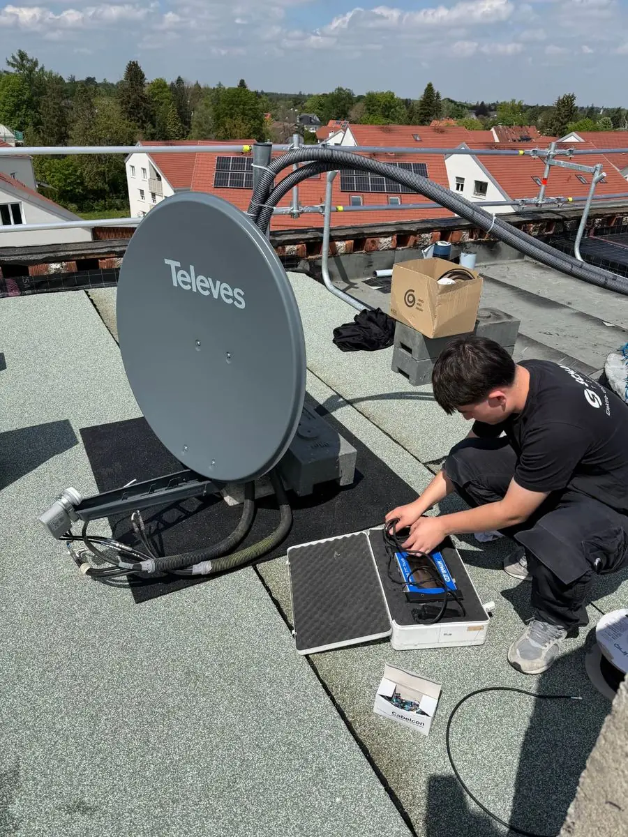 Monteur von Schauer Technik richtet eine SAT-Antenne auf einem Flachdach aus